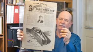 Steve Mayfield is a crime lab photographer and Mormon documentation collector. Here he is holding a newspaper from 1877 on John D. Lee execution.